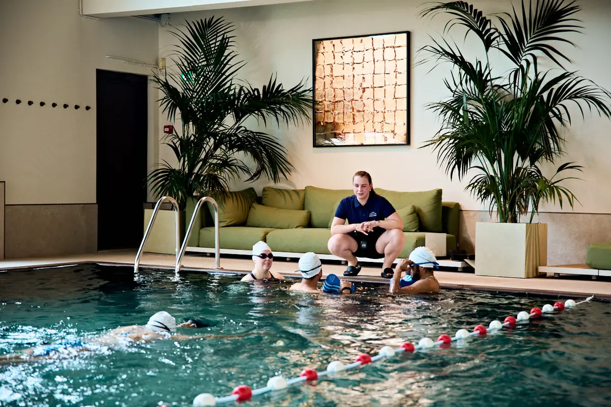 A coach crouches poolside, guiding a small group of swimmers at the wall